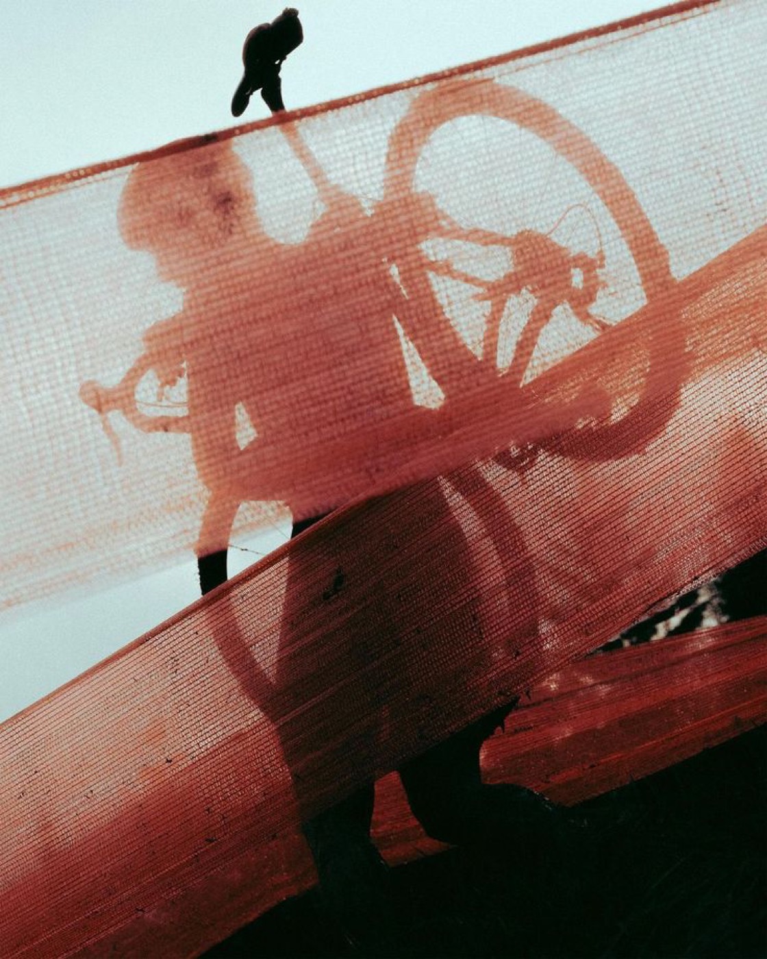 An athlete and bicycle seen through red mesh